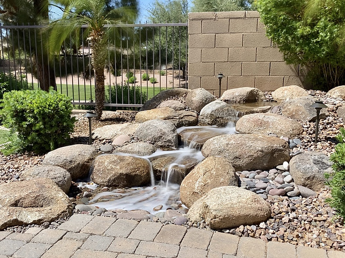 A pondless waterfall in a backyard surrounded by rocks