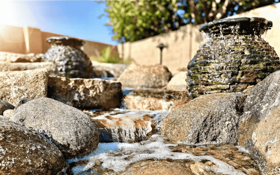 A small man-made creek in a backyard with multiple fountains designed into it.