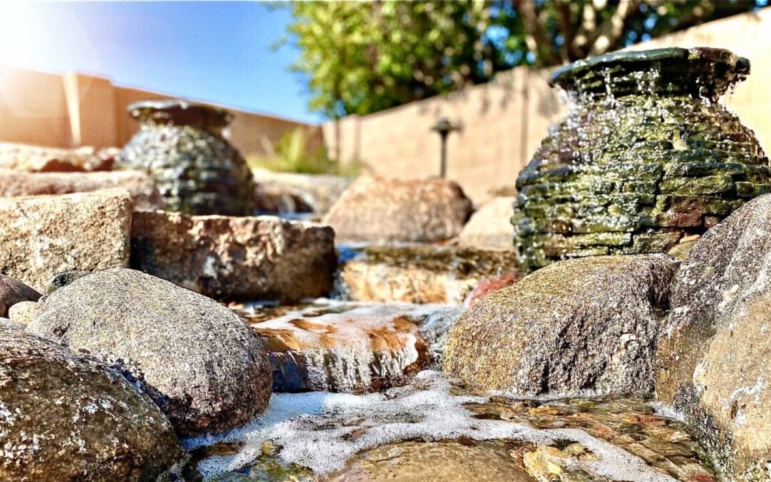 A small man-made creek in a backyard with multiple fountains designed into it.