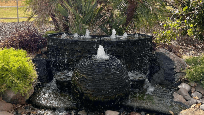 A black stone sphere-shaped fountain with a semi-circle fountain behind it.